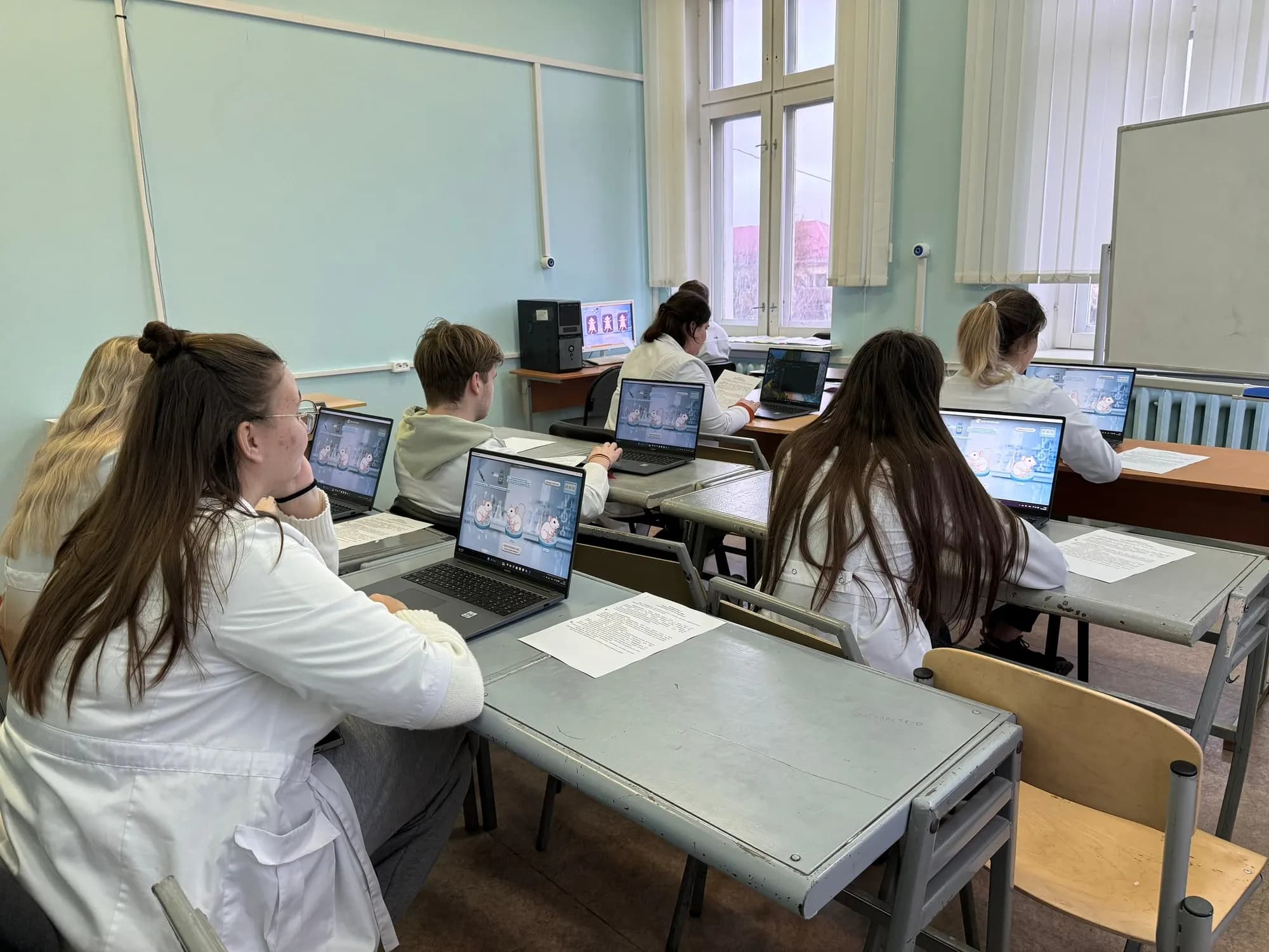 Занятие на кафедре: группа студентов в белых халатах проходит модуль на ноутбуках, рядом лежат методические рекомендации